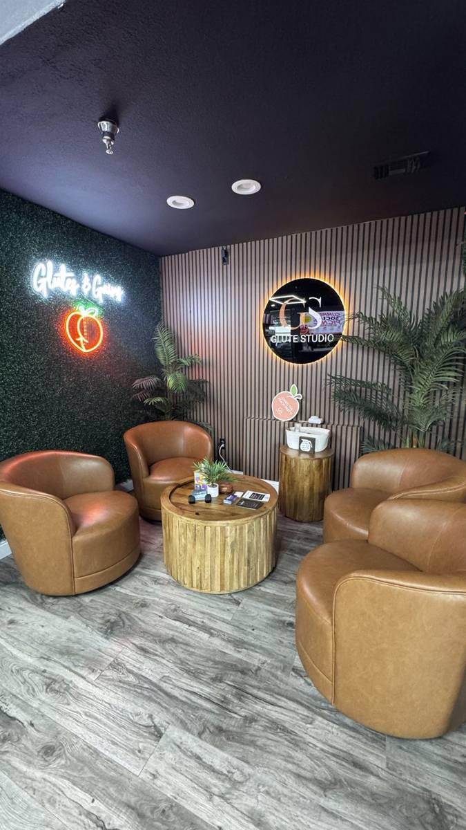 Glute Studio lounge with leather chairs, Glutes and Gains neon and lit GS sign